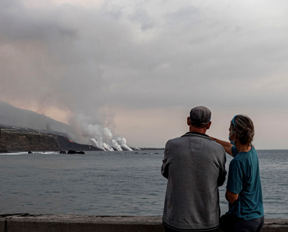 Unos turistas contemplan desde el puerto de Tazacorte la llegada al mar de la colada del volcán Cumbre Vieja